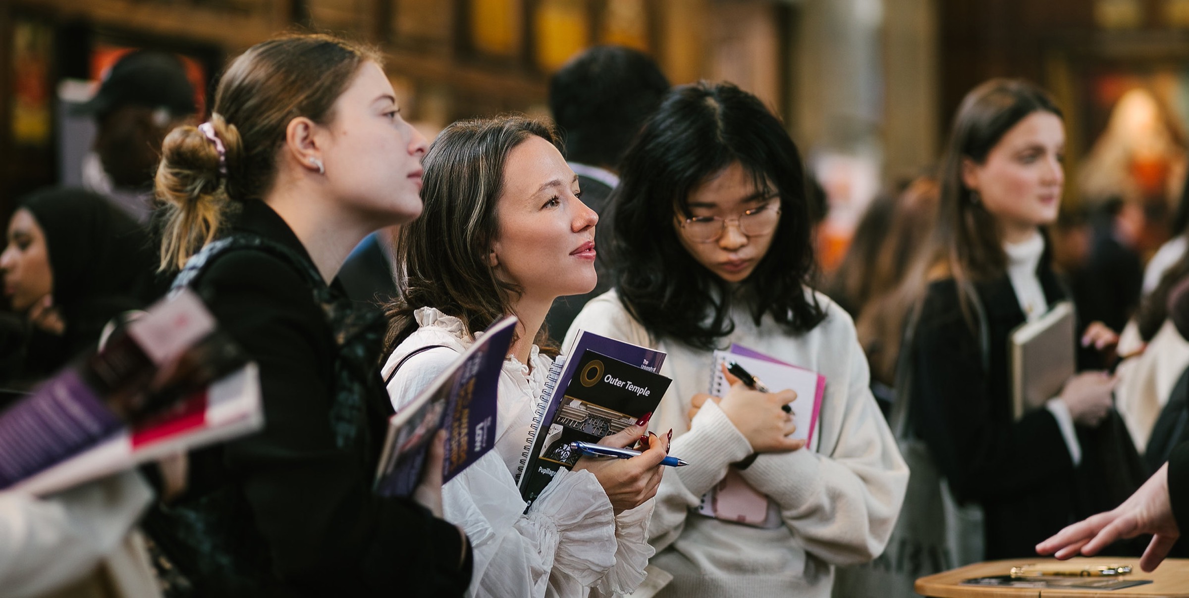 Students at a university careers fair holding prospectuses and notebooks